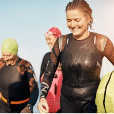 Group of cheerful swimmers in wetsuits, emerging from the water on a sunny day.